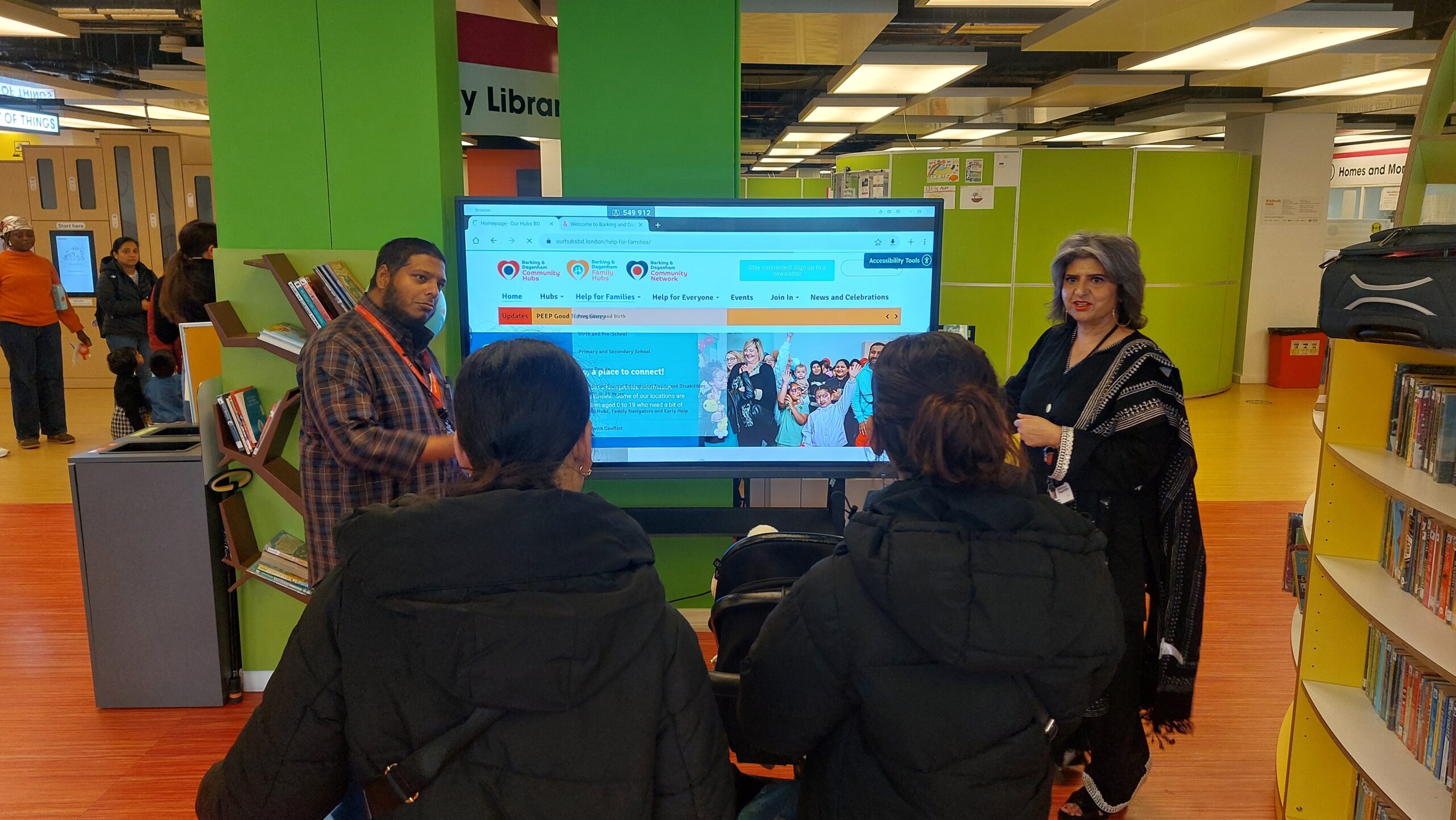 People gathered around a screen displaying a website in a library setting.